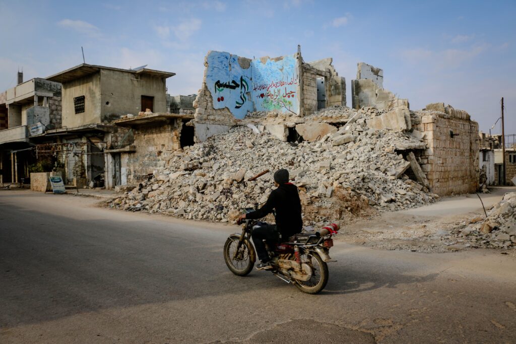 Idlib, Idlib Governorate, Syria. A man on a moped in front of a building in ruins