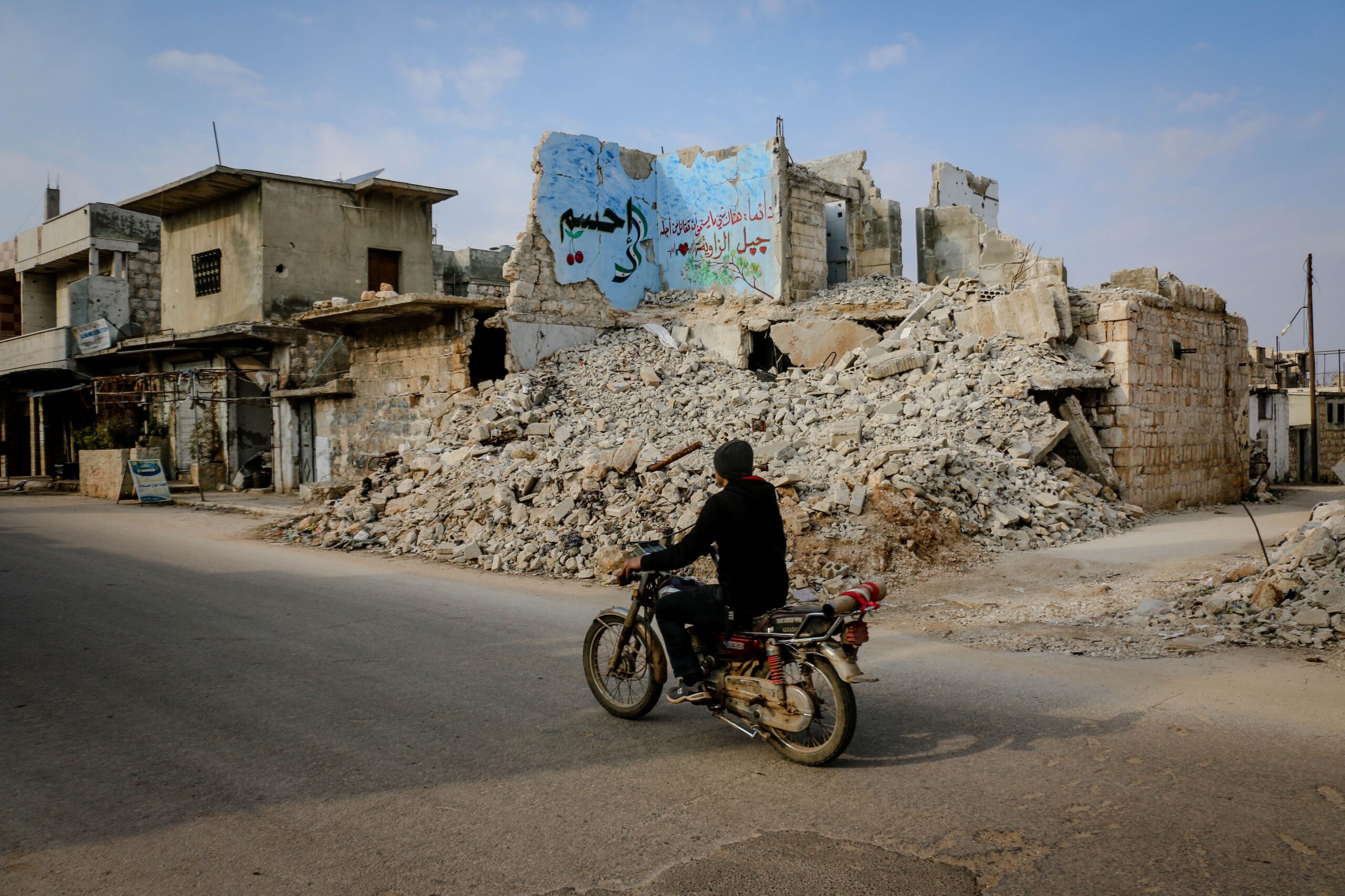 Idlib, Idlib Governorate, Syria. A man on a moped in front of a building in ruins